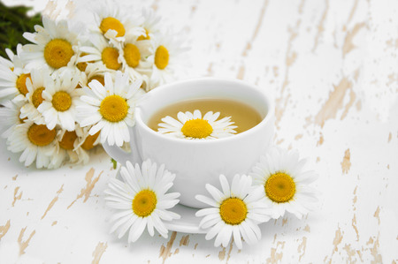 A cup of chamomile tea with a bouquet of daisies on a wooden backgroundの写真素材