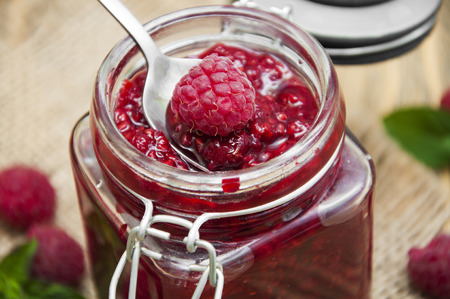 Raspberry jam with fresh raspberries on wooden background