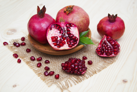 Fresh red juicy pomegranates in wooden plate with grains on a wooden backgroundの写真素材