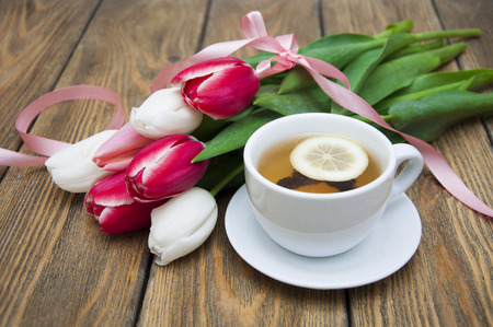 A cup of tea with lemon and colorful tulips on a wooden backgroundの写真素材