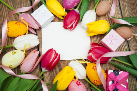 Gift card with colored Easter eggs with tulips and gift boxes on wooden backgroundの写真素材