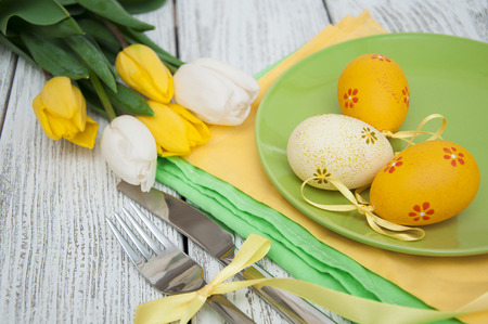 Easter background with yellow tulips and colorful eggs over white wooden table. Top view with copy spaceの写真素材