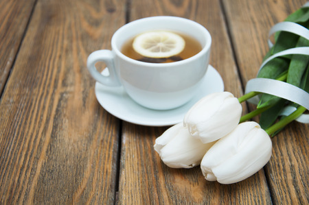 A cup of tea with lemon and white tulips on a wooden backgroundの写真素材