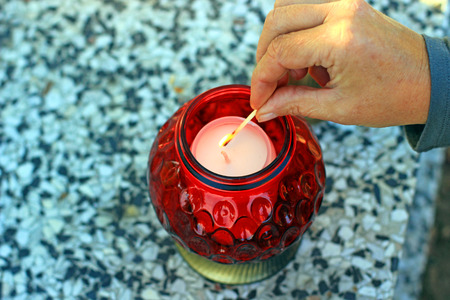 Woman at cemetery is lighting a red candleの写真素材