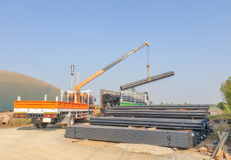 The crane lifts the steel structure off the truck in daytime.の写真素材