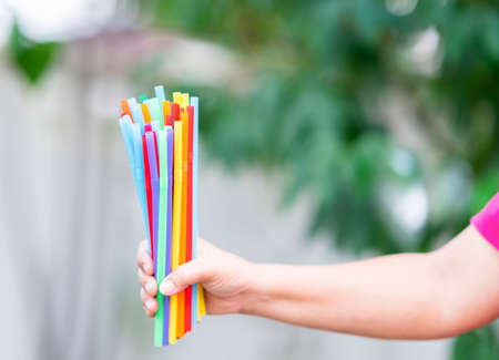 A colorful straw in the hand of a woman on out of focus background.の写真素材