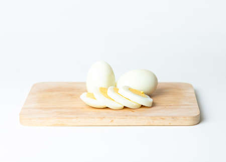 Two boiled eggs and egg slice on wooden board, isolated on white background.の写真素材
