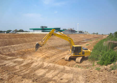 Back hoe is digging the ground to make a big pond behind the factory.の写真素材