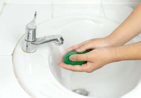 young man washing hands with soap on white basin.