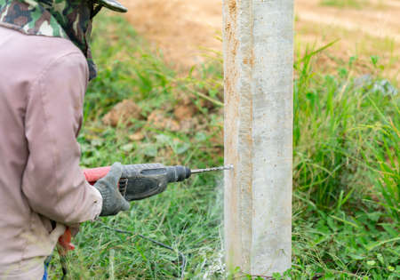 Workers drill cement columns to install support metal sheet for fences around the factory.