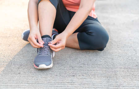 Woman sitting on a cement floor with shoelaces in front of her home.の写真素材