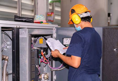 The engineer wears an ear muff while inspector the air compressor in factory.
