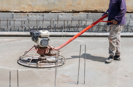 Worker with power trowel tool finishing concrete in construction siteの写真素材