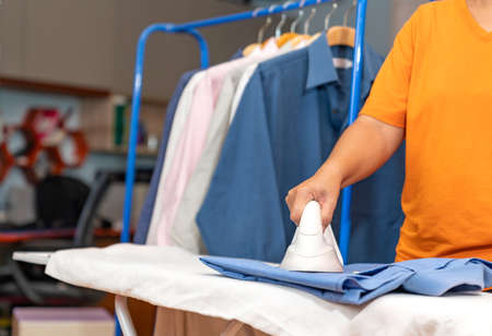 Woman ware orange shirt Ironing and hangon rail behind.の写真素材