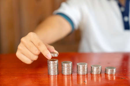 Man hand putting coin, stack on wooden table in the morning sunlight. business, investment,...