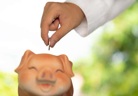 Businessman putting a coin in a brown piggy bank on out of focus background.の写真素材