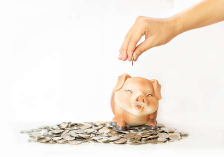 Man putting coin in piggy bank on pile coin money. Saving money concept.