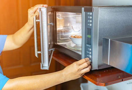 Woman putting bowl with food in microwave oven, closeup.