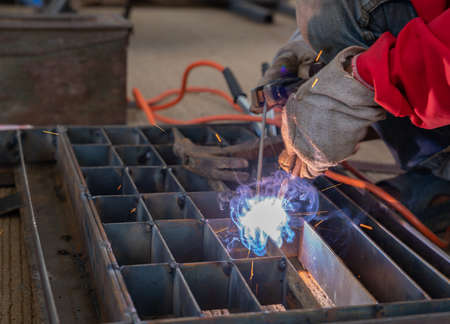 Worker ware gloves welding steel grill pipe cap and spark in factory.
