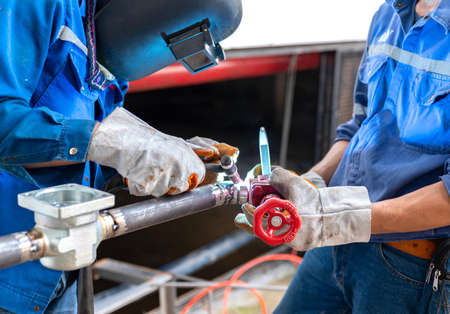 Worker in blue uniform,leather gloves,welding mask. welding the workpiece with a liquid line process