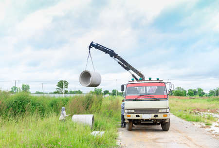 Worker use crain lift up concrete sewage pipes from truck put down on the ground prepare for underground instalation and blue sky background.の写真素材
