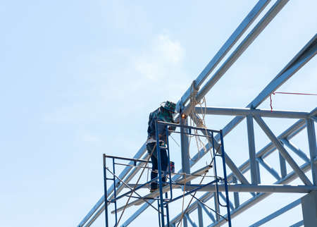 Low Angle View Of Welder Welding roof top Metal bar Against Clear Blue Sky