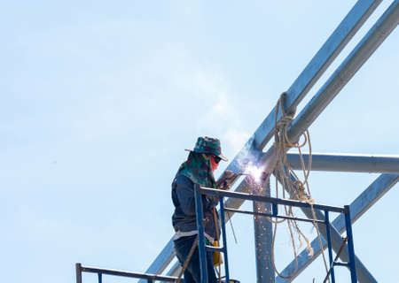 Worker welding pole structure for car park roof in factory.The iron was painted with grey rust-proof...