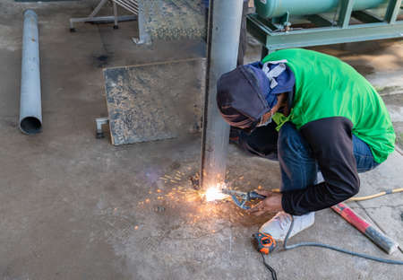 A welder welds a metal pole without gloves and mask holds an electrode in his hands in construction...