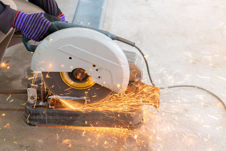 A worker uses a fiber cutter to cut a sparkling metal frame in factory.