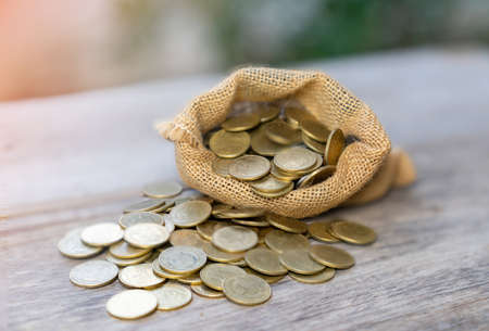 Gold coins overflowing from sack the saving concept for rich in the future on wooden desk in out of focus background.の写真素材