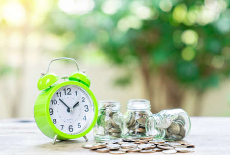 Time for pension planning saving money for future and retirement, Glass jar with coins and alarm clock on blurred background.の写真素材