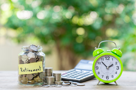A alarm clock,calculator and a coin in on wooden table with a blur background. Concept of saving money for retirement.の写真素材