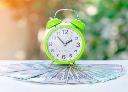 Alarm clock and dollar bills concept of time to make earn on blur background.の写真素材