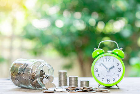 Plan life saving money insurance at retirement concept with coin stack, coin in jar and alarm clock on out of focus background.の写真素材