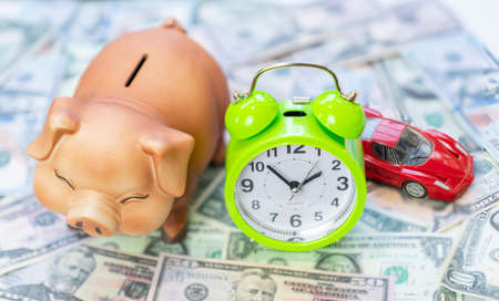 Concept Time to savings for car.Piggy bank with alarm clock and car model on background of money.の写真素材
