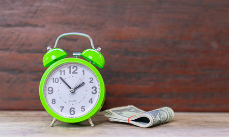 A time to make money as an important business resource. Green alarm clock and dollar bills on wooden background.の写真素材