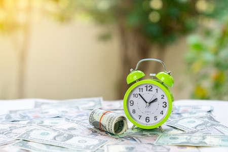 Alarm clock sit on dollar bills tired and pile on blur background. Concept to earn money and saving.の写真素材