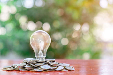 Light bulb sit on stacks of coins on out of focus background. Energy saving concept.の写真素材