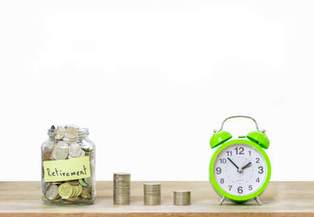 Concept saving and retirement.Coins in jar with money stack step growing money and alarm clock.の写真素材