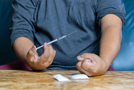 The man junkie hand trying to grab injection syringe of cooked heroine.の写真素材