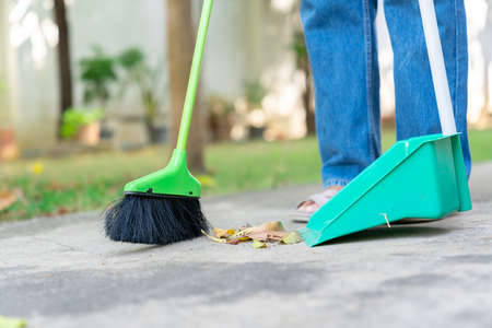 Woman is sweeping the floor and collecting the dried leaves on out of focus background.