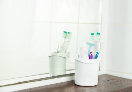 Two toothbrushes and toothpaste in basket on wooden shelf in bathroom.の写真素材