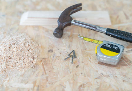 Hammer, nail and measure tape place near sawdust on the wooden table.の写真素材