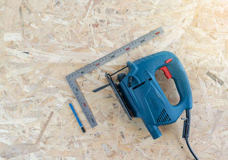 Pencil, ruler square and electric jigsaw paste on wood table in workshop.
