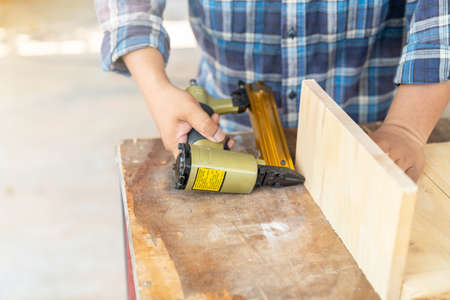 The carpenter using nail gun to nail wood board sheeting in workshop.の写真素材