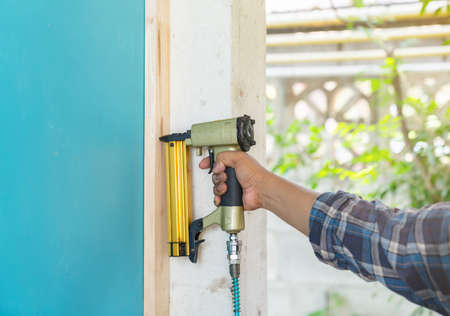 The carpenter with a air nail gun nailer working on wood frame of walls on a new home constructiion projectの写真素材