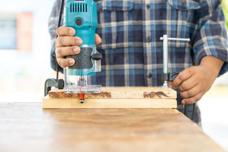 The carpenter using a electric trimmer to cut edging wooden board in workshop.の写真素材