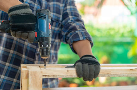 Carpenter working with cordless screwdriver finish furniture on out of focus background.の写真素材