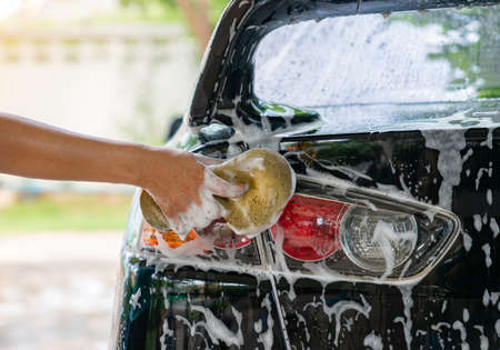 Woman washing car tail lights with shampoo at home. Car detailing concept.の写真素材