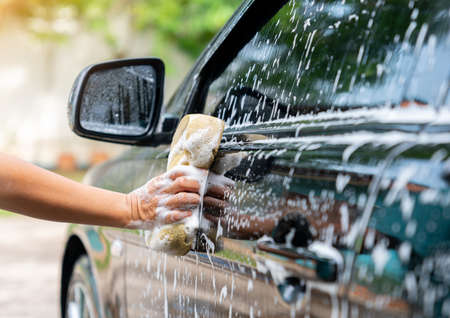Woman hands hold sponge for washing car at home. Car detailing concept.の写真素材